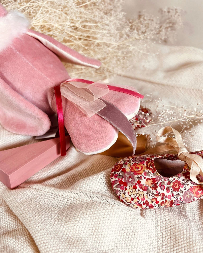 Pink velvet tail and a floral-patterned shoe on a textured surface