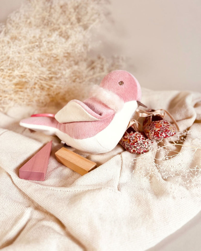 Pink and white bird-shaped baby plush toy on a textured beige surface
