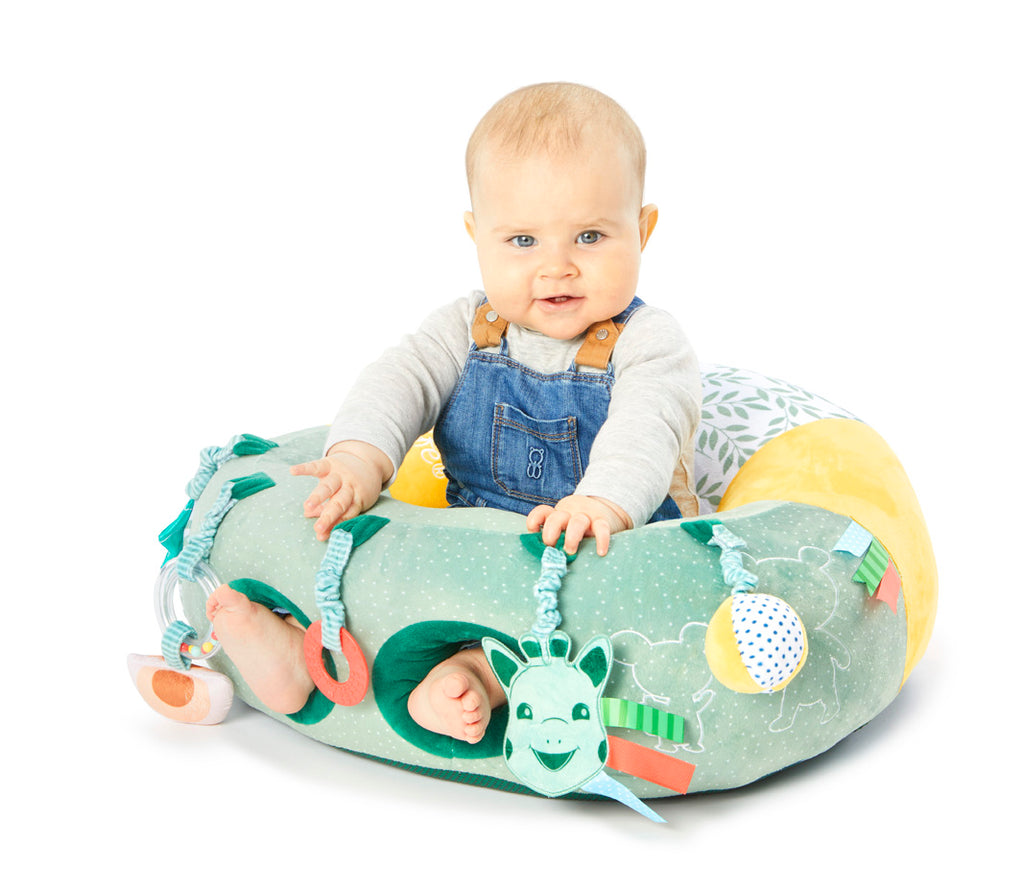 A baby sitting in a soft, Sophie the Giraffe baby seat with toys