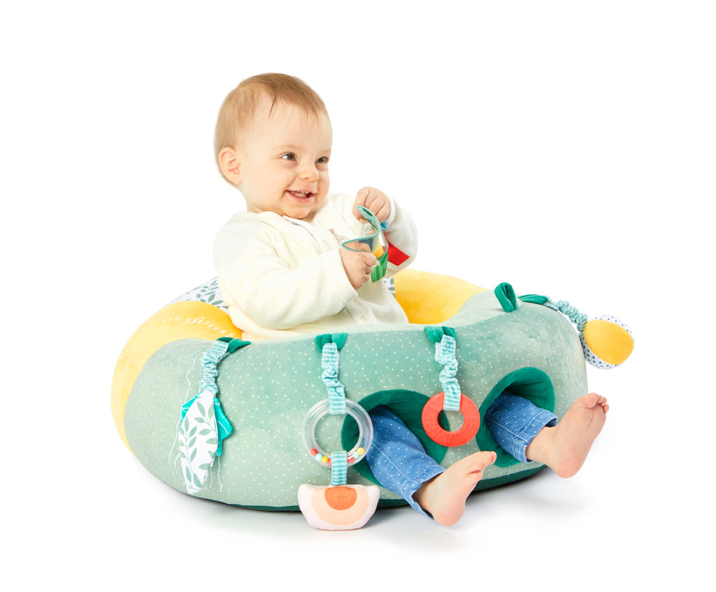 A smiling baby playing with the Sophie the Giraffe baby seat