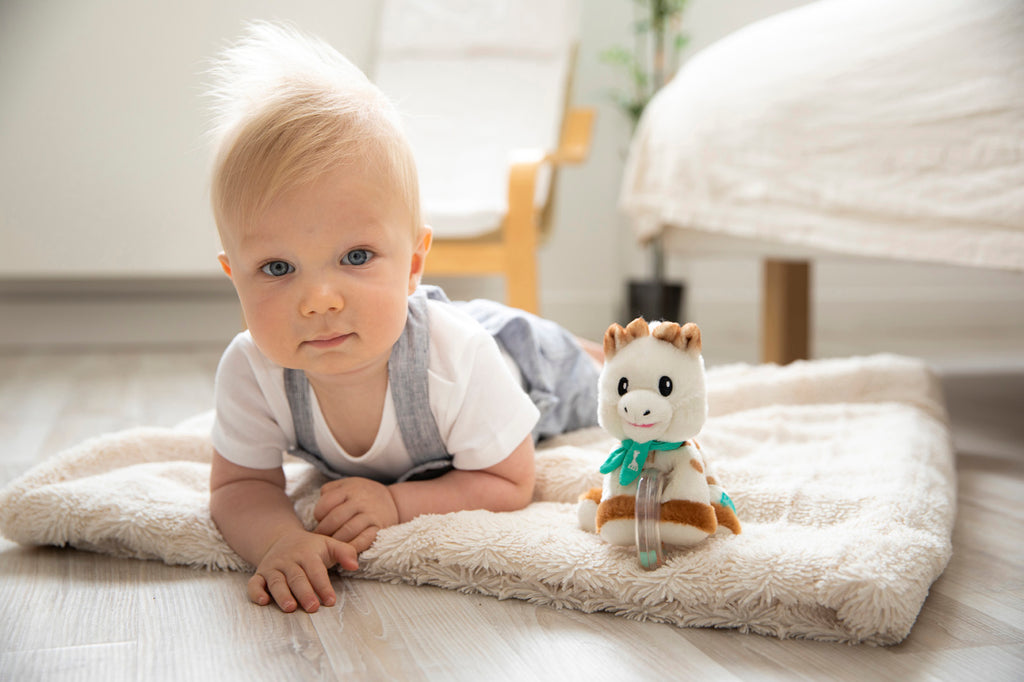 Baby laying next to sophie plush with beads